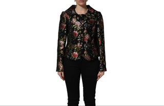 A model wearing a black long-sleeve floral jacket with pink and gold accents, paired with black pants, shown against a plain white background.
