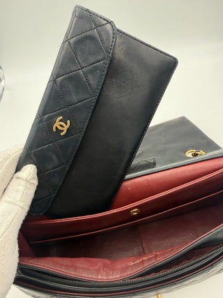 Two leather handbags, one black quilted with gold logo and one red, on a light gray background.