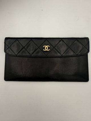 Black quilted clutch bag with gold Chanel logo on a light gray background