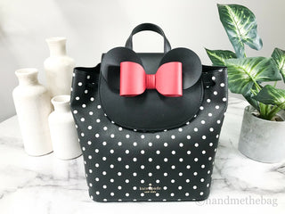 Black polka dot handbag with a pink bow on a marble surface with decorative vases and plants.