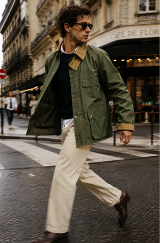 Man walking on a city street wearing a green jacket and sunglasses.