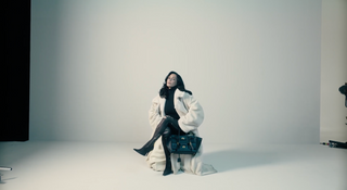 Person in a white coat sitting on a white floor with a plain background