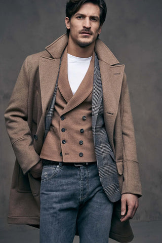Man wearing a brown coat over a plaid vest with a plain background