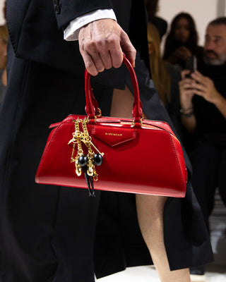 Red Givenchy handbag held by a person at a fashion event.