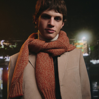 Person wearing a brown coat and orange scarf against a dark background
