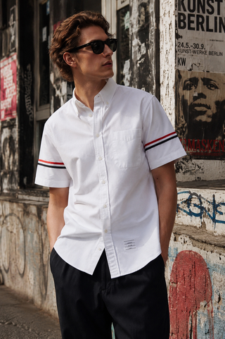 Man wearing a white short-sleeve shirt with red and blue stripes against a graffiti-covered wall.