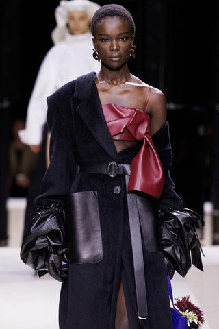 Model wearing a black coat with a red top on a runway