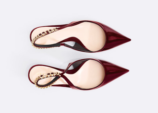 A pair of pointed-toe slingback flats in glossy burgundy patent leather, featuring a decorative gold chain embellished with small dark stones across the slingback strap, shown against a light gray background.