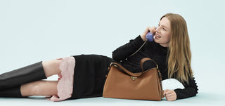 Woman lying on a light blue surface with a brown handbag next to her