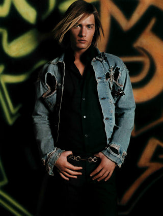 Person wearing a distressed denim jacket in front of a graffiti wall