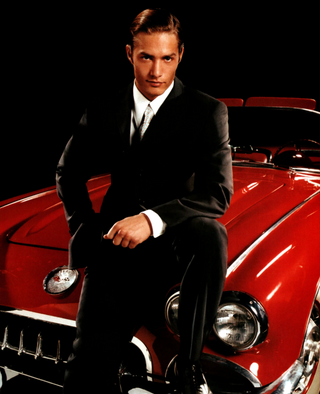Man in a suit sitting on a red classic car against a black background