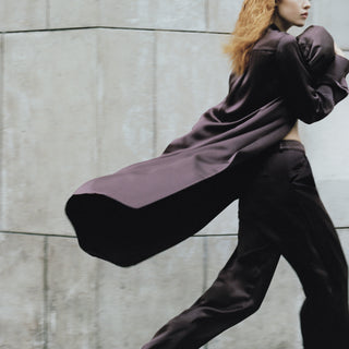 Person wearing a long, flowing dark outfit against a concrete wall.