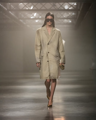 Model walking on a runway wearing a beige trench coat.