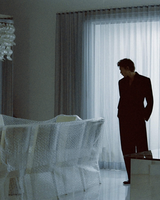 Man standing in a modern dining room with white chairs and a chandelier.