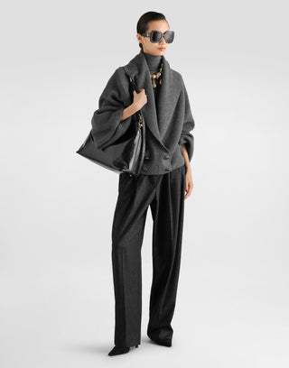 A model wearing a dark gray double-breasted coat, matching wide-leg trousers, a dark gray turtleneck, black sunglasses, and carrying a large black leather shoulder bag against a light gray studio background.