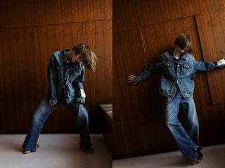 Person wearing a denim jacket and jeans against a wooden paneled wall.