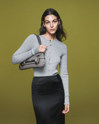 A women in a grey Top holding a grey shoulder bag