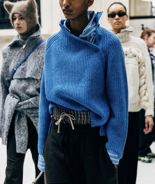 Person wearing a blue sweater with a patterned belt, standing in a crowd.