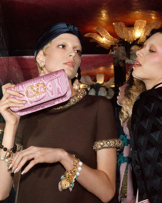 Two women in a social setting with one holding a pink Gucci clutch.