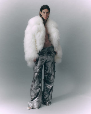 Person wearing a white fur coat and patterned pants on a plain background