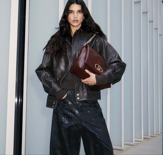 Person wearing a black leather jacket and holding a brown leather bag in an indoor setting.